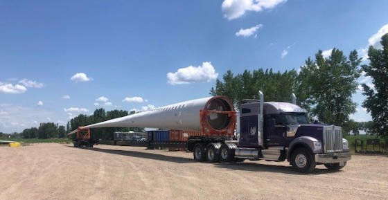 A purple FT&L tractor hauling a wind turbine blade across a staging yard