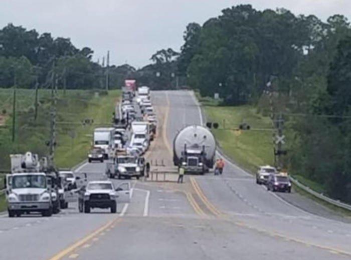 A long escorted convoy holding traffic on a two-lane rural highway