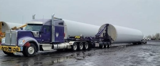 An FT&L driver in a high-visibility safety vest standing beside a purple truck