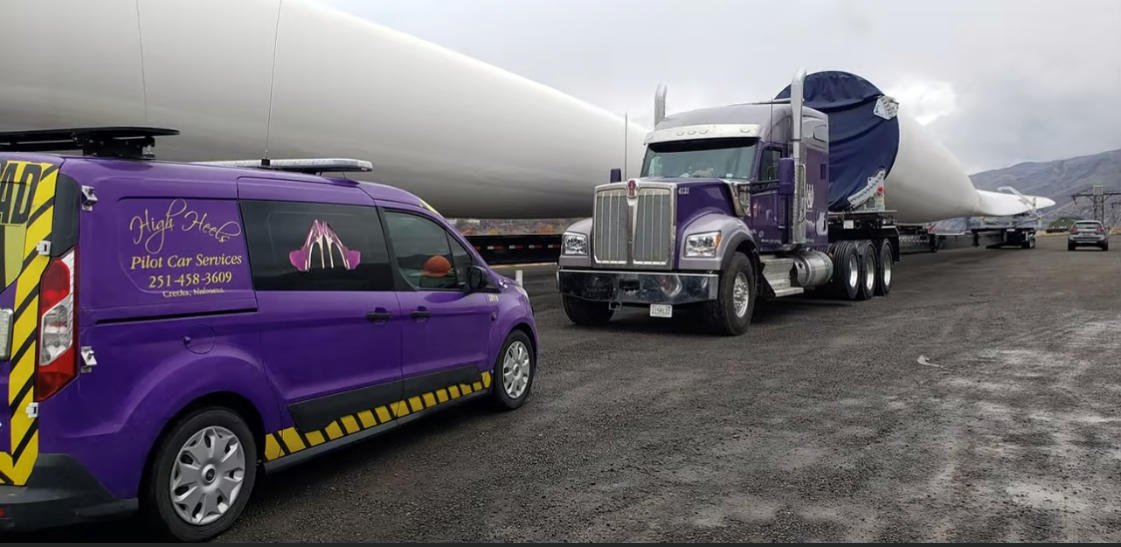 A purple FT&L tractor with a tower section staged on a roadside shoulder