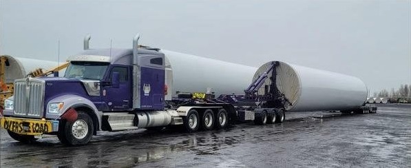 A purple tractor with a blade root secured on a lowboy trailer at a wet staging lot