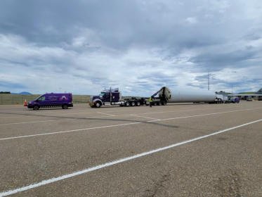 Turbine blade loaded on a specialized trailer staged on a road shoulder
