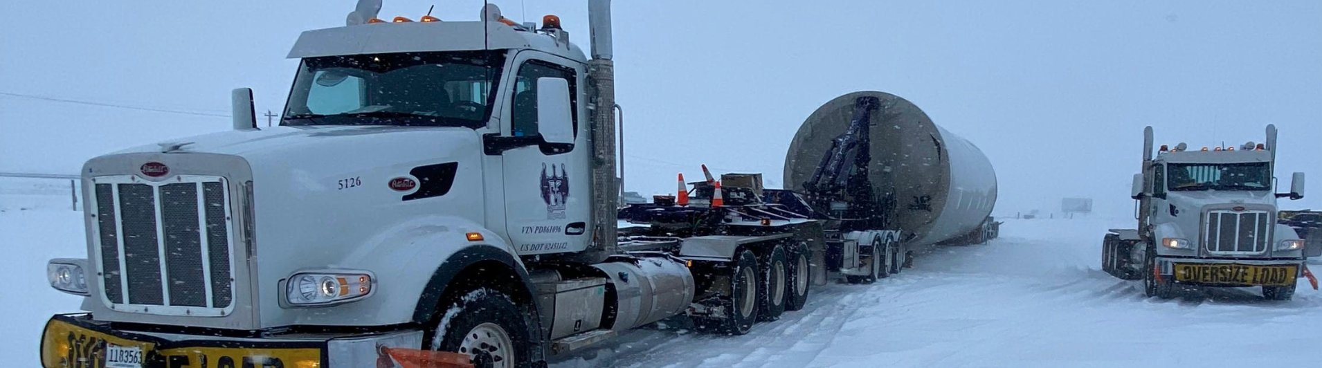 Purple FT&L Specialized escort van and Peterbilt tractor staged with a white wind turbine component on the trailer