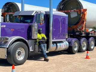 FT&L driver in a high-visibility safety vest standing beside his purple Peterbilt
