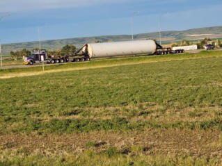 Purple FT&L tractor-trailer carrying a large tower section along a road past an open field