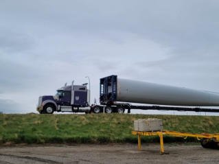 Purple FT&L tractor hauling a turbine blade along a rural highway