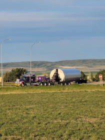 FT&L truck with an oversize load crossing a road past a green field