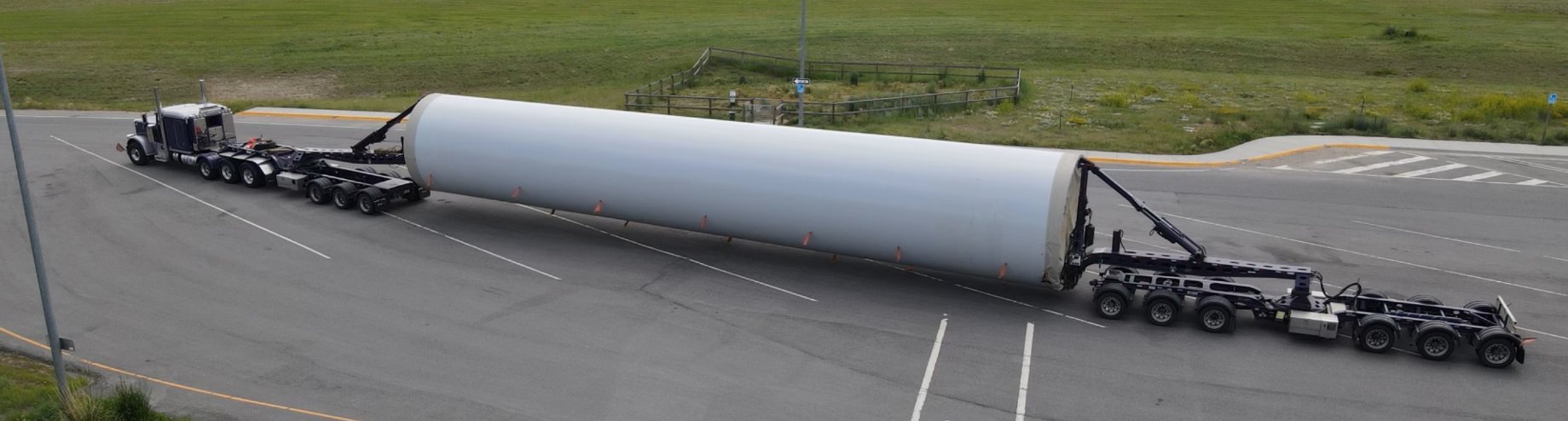 A wind tower section on an extended trailer sweeping through a highway curve
