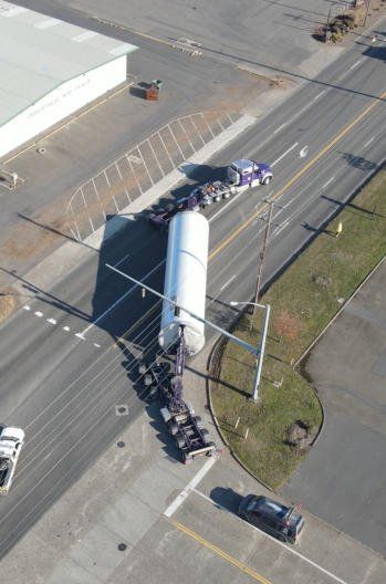 Aerial view of an extended wind tower load turning through a town intersection with escorts