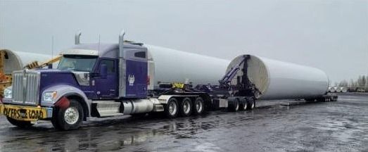 An FT&L driver in a high-visibility safety vest standing beside a purple truck