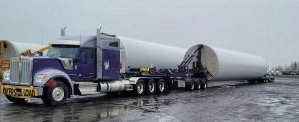 A purple tractor with a blade root secured on a lowboy trailer at a wet staging lot